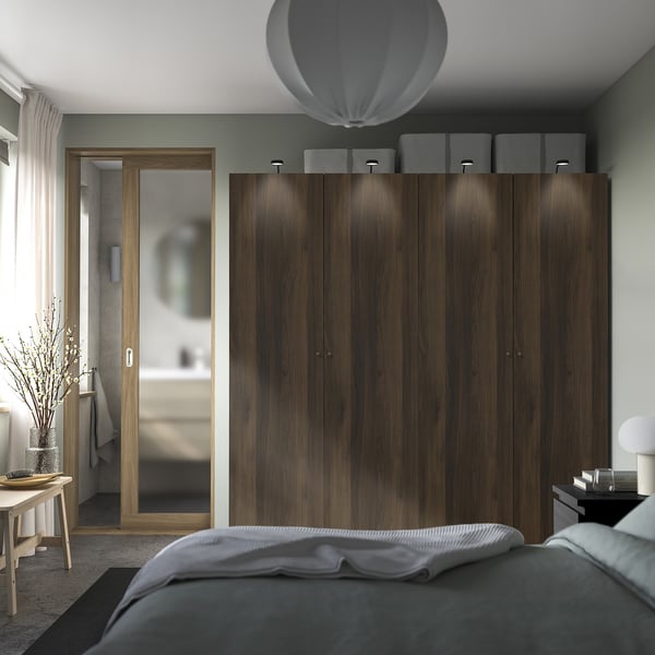 A modern bedroom with a large dark brown PAX wardrobe, ceiling-high, featuring integrated lighting and a large mirror.