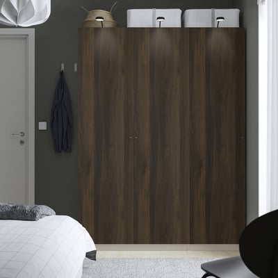 Modern bedroom with large dark wood PAX wardrobe. Wardrobe towers above bed, gray wall, white decor.