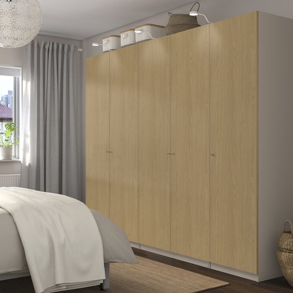 Large PAX closet in light wood stands tall beside bed, matching modern decor with ample storage.