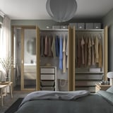 Modern bedroom with wooden wardrobe showcasing clothes, hanging rail, and storage baskets.