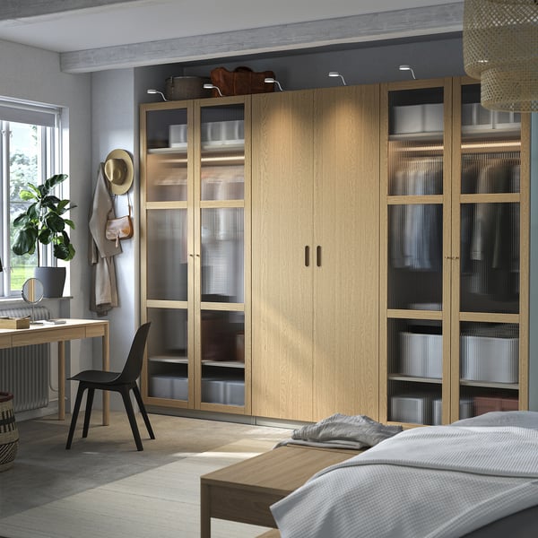 Modern bedroom with ikea PAX wardrobe, mix of solid and glass doors, near window with desk and chair.