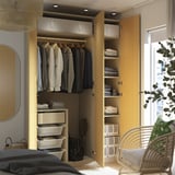 Open wooden wardrobe showing clothes, folded towels, and storage bins. Integrated lighting illuminates the interior.