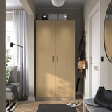 Modern bedroom with tall wooden wardrobe, gray chair, black lamp, and mirror by white door.