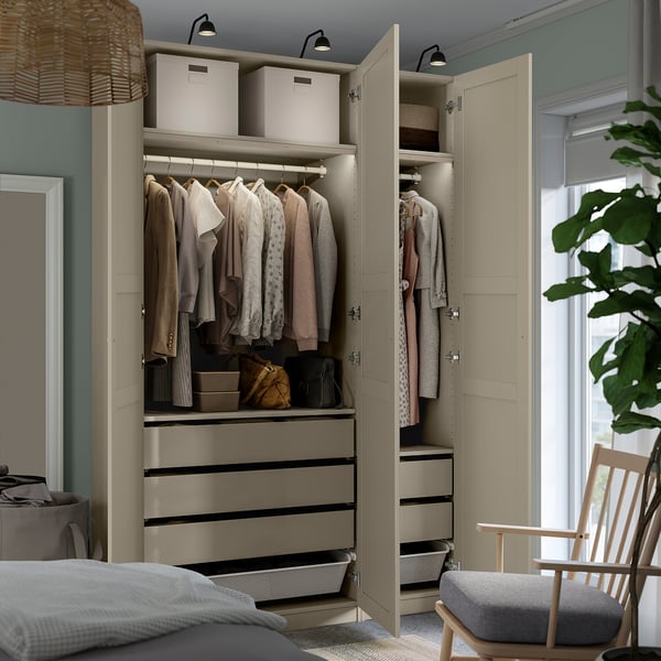 Bedroom with open wardrobe showing clothes, bags, and storage drawers. Wardrobe has adjustable feet and integrated lighting.