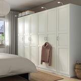 A white PAX wardrobe with multiple sections, larger than the bed beside it. It hangs a sweater and has stylish handles.
