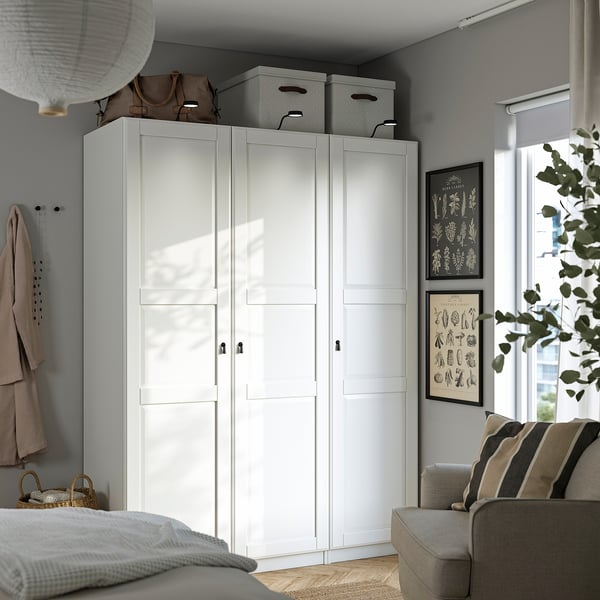 White PAX wardrobe, gray wall, beige sofa, frosted doors, gray boxes, hooks, basket, bright room, window, plant.