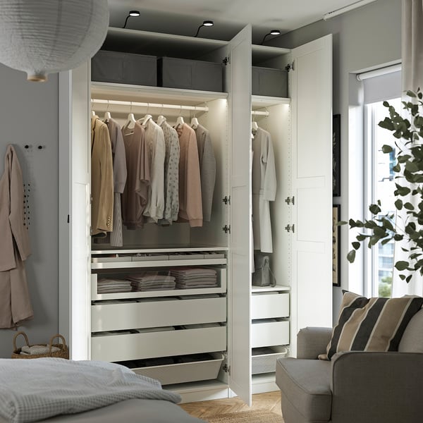 Modern bedroom with PAX wardrobe, hanging clothes, drawers, and lighting.