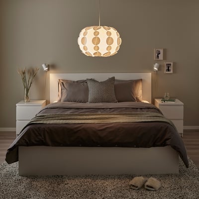 Modern bedroom with brown-beige tones. PEKTOLIT lamp above bed, bedside tables, rug, slippers, framed pictures.