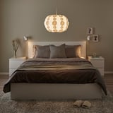 Modern bedroom with a large bed, dark bedding, and a prominent PEKTOLIT pendant lamp with a circular shade, creating a cozy atmosphere.