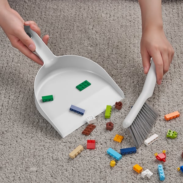 Person cleaning colorful blocks from carpet with dustpan and brush.