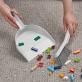 Person cleaning colorful blocks from carpet with dustpan and brush.