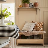 Cozy room with pine bench, floral pillows, plants, and checkered cloth.