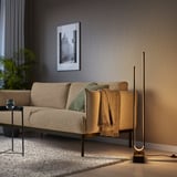 Modern living room with PILSKOTT floor lamp, beige sofa, and plant. Lamp has a sleek, tall, black design with warm lighting.