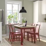 Red PINNTORP dining set with pine table & chairs fits cozy spaces. Tabletop with laptops and flowers, white kitchen cabinets in background.