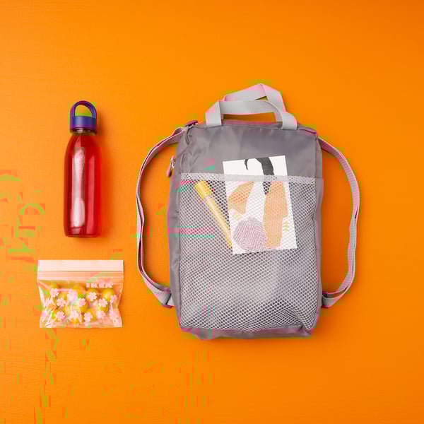 Gray PIVRING backpack with mesh front pocket, red water bottle, and clear IKEA snack bag on orange background.