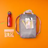 Gray PIVRING backpack with mesh front pocket, red water bottle, and clear IKEA snack bag on orange background.