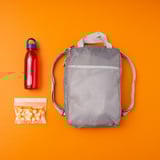 Gray polyester backpack with bottle & snacks in mesh pocket, orange backdrop.