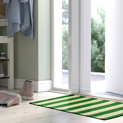 Green room with white floors, glass doors, and a striped rug at the entrance.