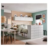 Modern bedroom with a PLATSA bed. White bed frame with storage, green painted walls. A desk with chairs, and a large window with blinds.