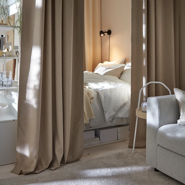 Cozy bedroom with beige PLATSA bed, white linens, gray chair, and open shelving unit with plants.