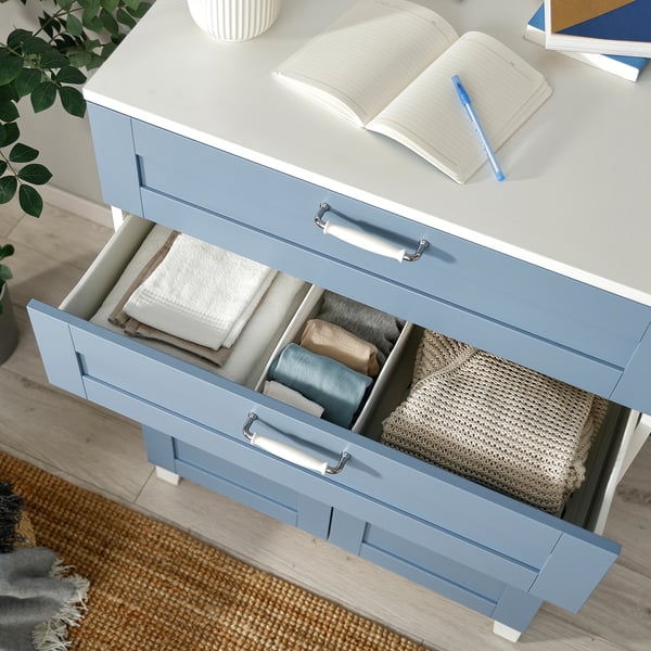 Open blue PLATSA drawer with folded clothes, organized with compartments, on a wooden floor.
