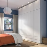 Large, white PLATSA wardrobe spans wall, towering over bed with orange blanket, fitting room neatly.