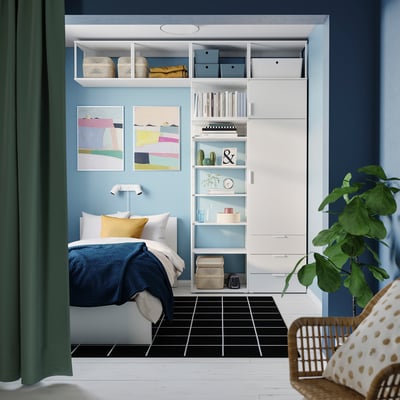 Modern minimalist bedroom: white PLATSA storage unit, blue accents, colorful art, cozy bedding.