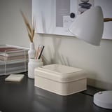 Small white PLOGFÅRA box on a desk, next to a lamp and pens. Organizer fits well with other desk items.