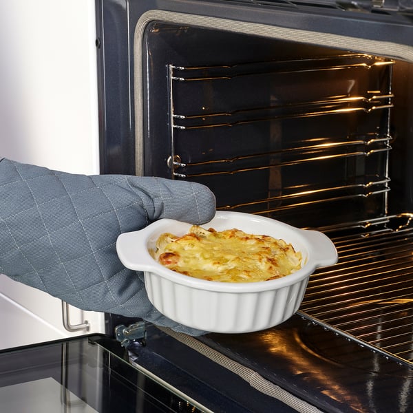 Hand holding a small oven dish with food, ready to be placed in oven. Dish has handles for easy lifting.