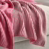 Pink striped blanket with soft, textured knit pattern draped over bed.