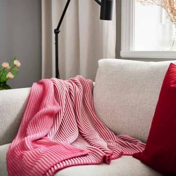 Red & white striped throw on grey couch with lamp & flowers.