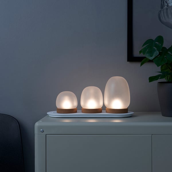 Three small table lamps on a white tray, emitting warm, flickering light, positioned on a blue surface.