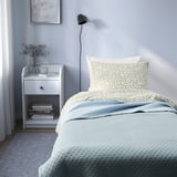 Blue PRAKTVIAL quilt on bed, soft & recycled, fits well, beside white nightstand.