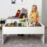 Kids play with toy car track set on table, including construction vehicles and signs, promoting creativity and motor skills.