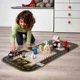 Child playing with RÄVUNGE car track set, positioning cars on a detailed road layout with houses and signs, enhancing creativity and motor skills.