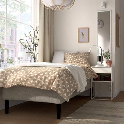 Minimalist bedroom with beige tones, low bed, mirror, nightstand, chandelier, window.