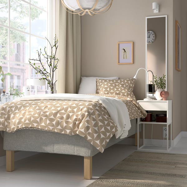 Modern bedroom with RÅHOLMAR bed, neutral decor, bedside lamp, plants, city view.