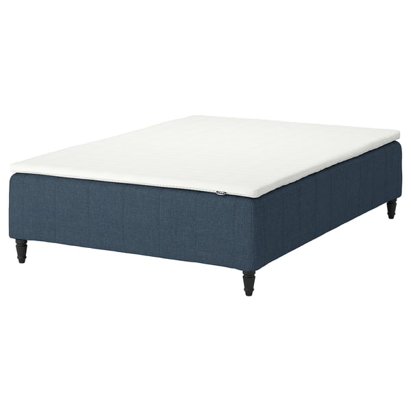The IKEA RÅHOLMAR bed base is upholstered in blue fabric with wooden legs and supports a white mattress.
