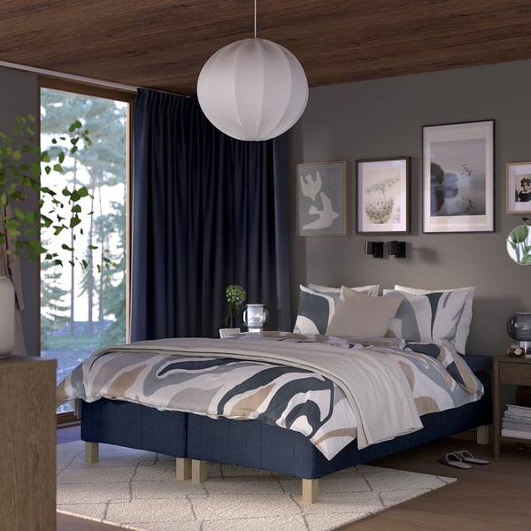 Modern bedroom with RÅHOLMAR bed, patterned mattress, wall art, dark blue curtains, rug, pendant light.