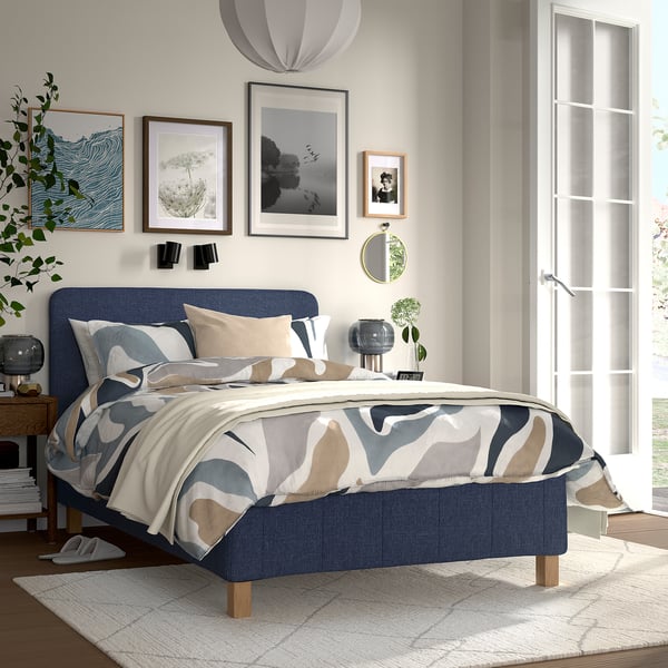 Cozy bedroom with blue RÅHOLMAR bed, abstract comforter, wall art, and large window.