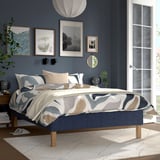 Modern bedroom with RÅHOLMAR bed, blue/white comforter, stylish decor, tv, large window.