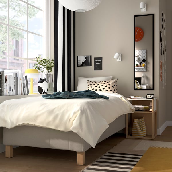 Modern bedroom with large window, white bed, polka-dot pillow, and plants.