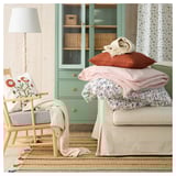 Bright living room with RAKLEV jute rug, green cabinet, white curtains, armchair, throw pillows in floral and stripes, lamp, blanket.