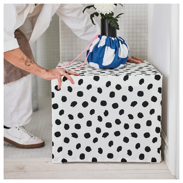 Person measuring fabric-covered box with dots; blue bag with flowers on top.