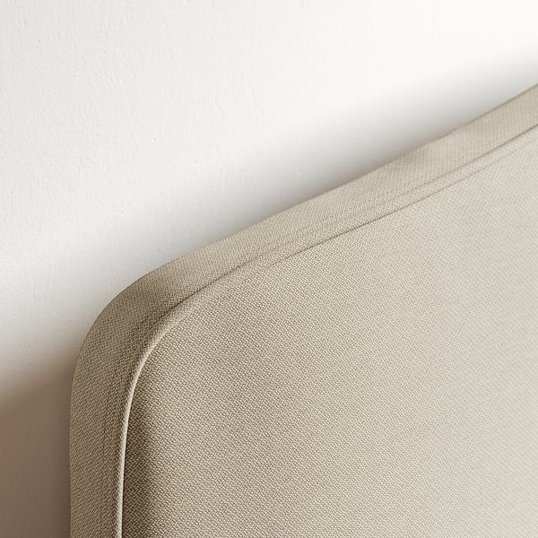 A close-up of a high-quality, beige fabric corner of a modern bed with neat stitching.