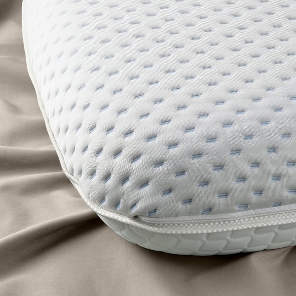 Close-up of ergonomic pillow showcasing its textured, breathable mesh surface atop a cozy bed setting.