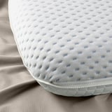 Close-up of ergonomic pillow showcasing its textured, breathable mesh surface atop a cozy bed setting.