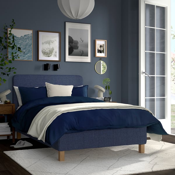 Modern blue bed in room with dark walls. Large white door, art on walls, layered bedding.