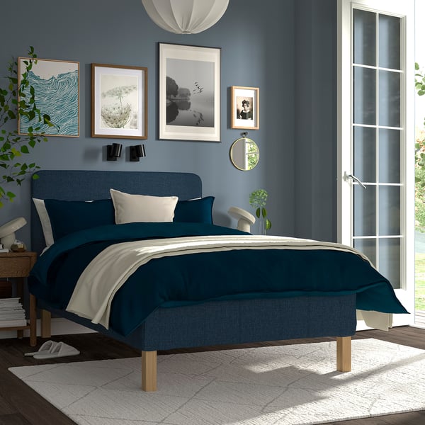 Modern bedroom with blue RENFJÄLLET bed, teal bedding, art, mirror, and green plant.