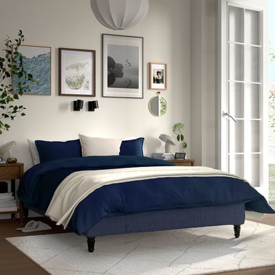 Modern bedroom with RENFJÄLLET bed, art, window. Wood frame, soft comforter, rugs, plants. Simple decor.